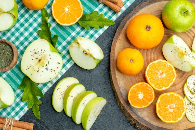 Free photo top view cut apples and tangerines on rustic round board cinnamon sticks on green tablecloth