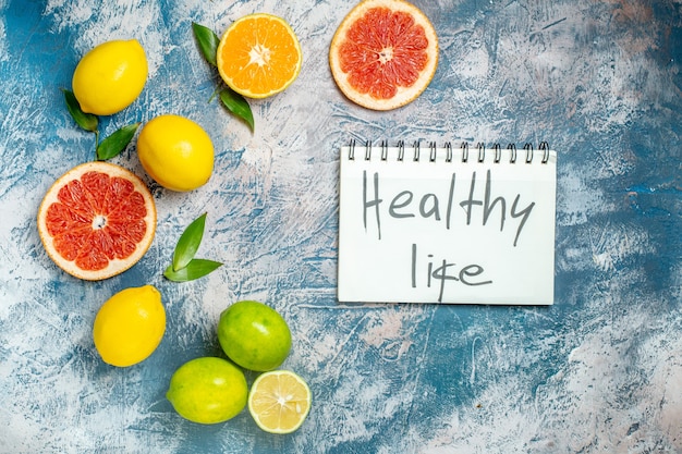 Top view cut grapefruits lemons healthy life written on notepad on blue white surface