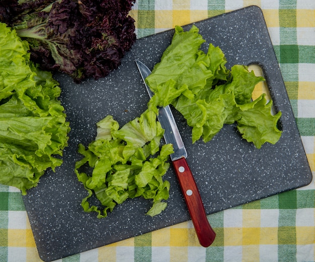 Free photo top view of cut lettuce with knife on cutting board and whole one with basil on plaid cloth