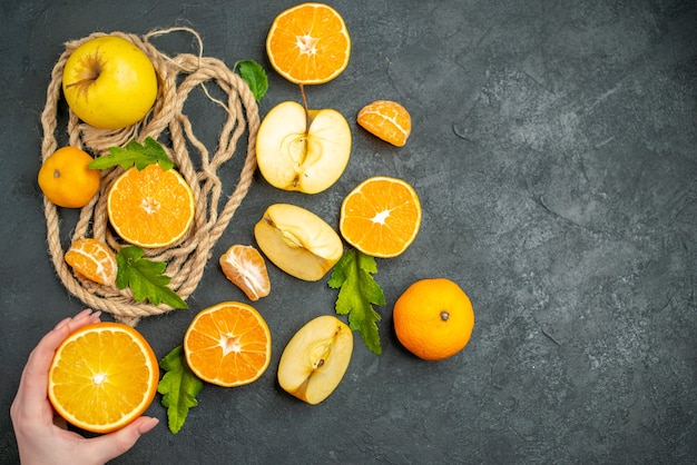 Top view cut oranges and apples cut orange in female hand on dark surface