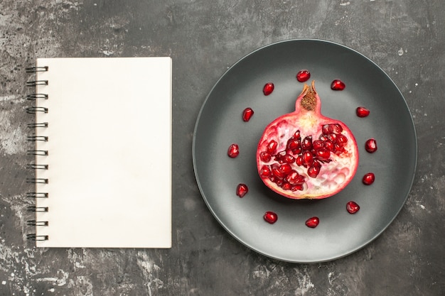 Free photo top view cut pomegranate on oval plate a notebook on dark background