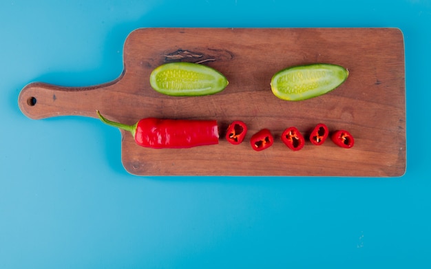 Free photo top view of cut and sliced vegetables as pepper and cucumber on cutting board and blue surface with copy space