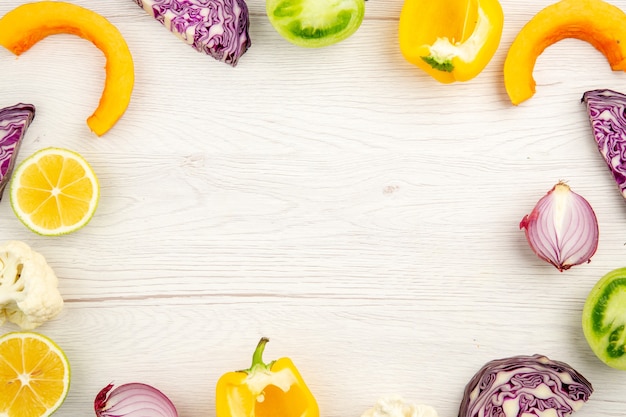 Top view cut vegetables red cabbage green tomato pumpkin red onion yellow bell pepper caulifower lemon on white wooden surface with free place