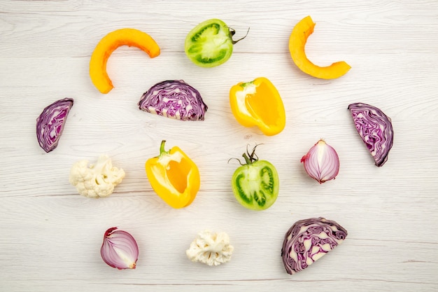 Top view cut vegetables red cabbage green tomato pumpkin red onion yellow bell pepper caulifower on white wooden surface