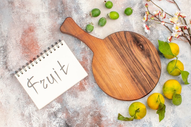 Free Photo top view a cutting board mandarines feykhoas fruit written on notebook on nude background