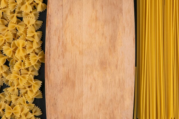 Top view of cutting board with raw pasta and spaghetti on a black surface