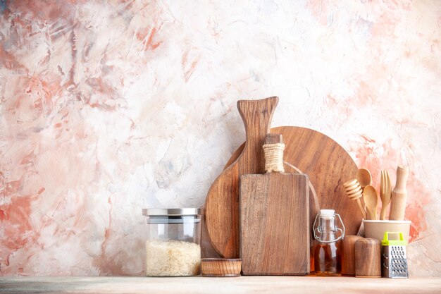 Top view of cutting board wooden spoons grater kumquats with stem in pot and rice in glass on colorful surface