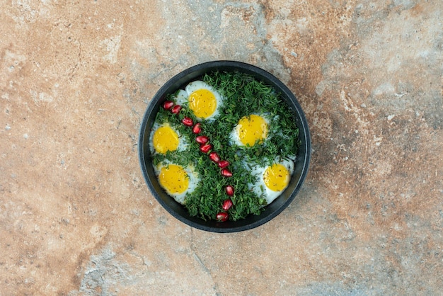 Top view of dark pan with omelet and greens .