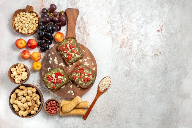 Top view of delicious avocado sandwiches with grapes and nuts on white surface