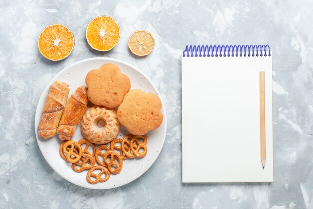 Top view delicious bagels with cookies crackers and cakes inside plate on light-white desk.