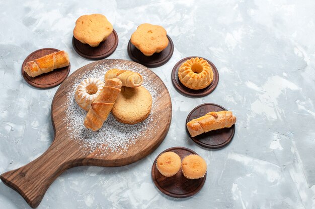 Top view delicious bagels with little cakes and cookies on light white background.