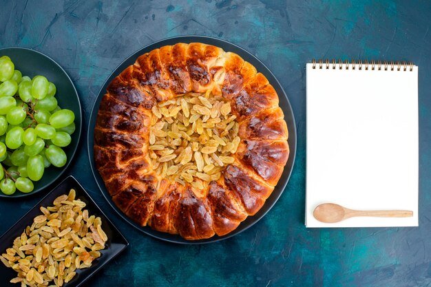 Top view delicious baked cake with raisings and fresh green grapes on the dark-blue background cake pie sugar sweet biscuit dough