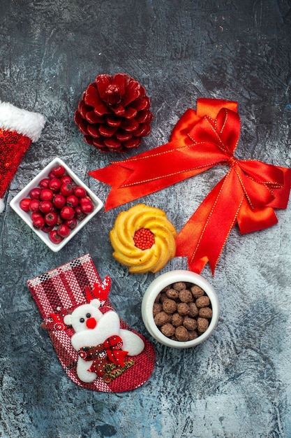 Free Photo top view of delicious biscuits and cornel on a white plate new year sock red conifer cone red ribbon santa claus hat on dark surface