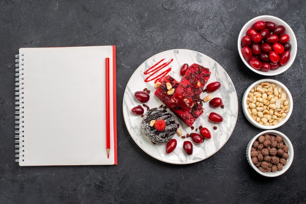 Top view delicious cake slices with nuts and dogwoods on grey desk