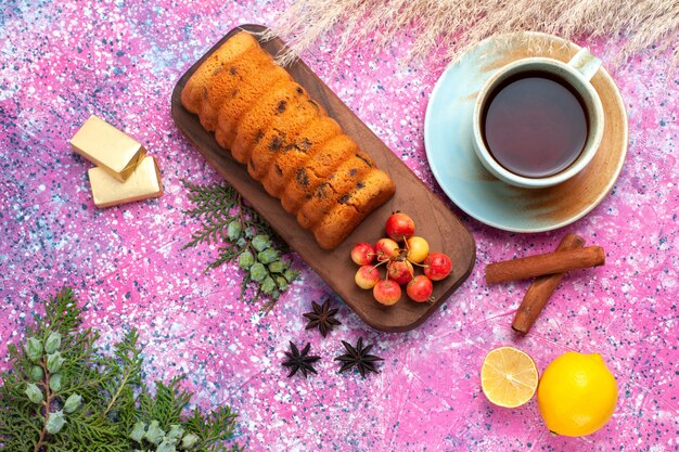 Top view delicious cake sweet and yummy with sweet cherries cinnamon and cup of tea on the pink desk.