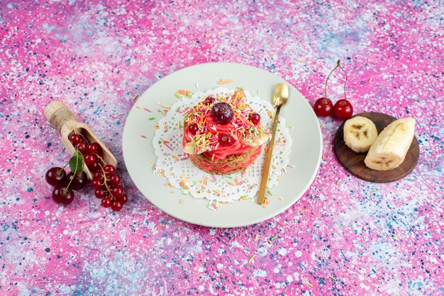 Top view delicious cake with candies banana and cherries on the colored background biscuit sugar sweet dough bake