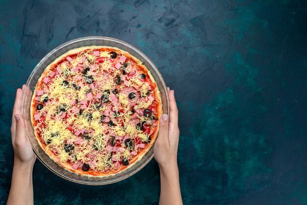 Top view delicious cheese pizza with olives tomato sauce sausages inside glass pan on light-blue background.