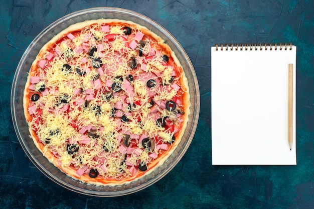 Free photo top view delicious cheese pizza with olives tomato sauce sausages inside glass pan with notepad on light-blue desk.