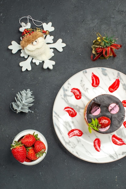 Free Photo top view delicious cheesecake with strawberry and chocolate on oval plate bowl of strawberries xmas toys on dark background