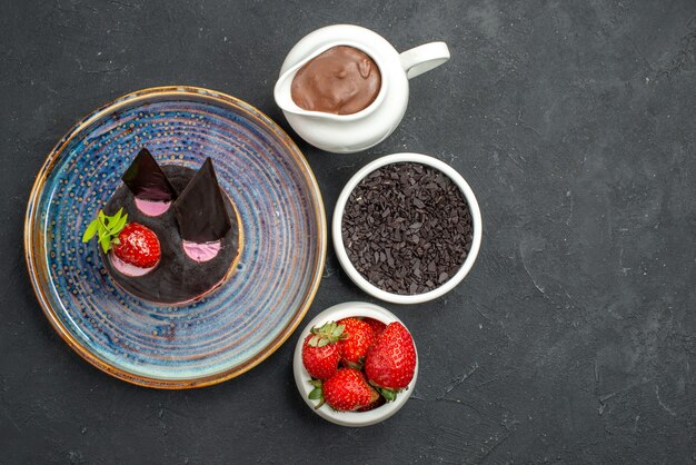 Free photo top view delicious cheesecake with strawberry and chocolate on plate bowls on dark isolated background