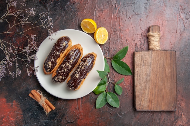 Top view delicious choco eclairs inside plate on dark table cake pie sweet dessert