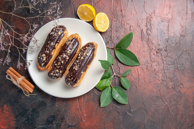 Top view delicious choco eclairs inside plate on a dark table dessert sweet cake pie