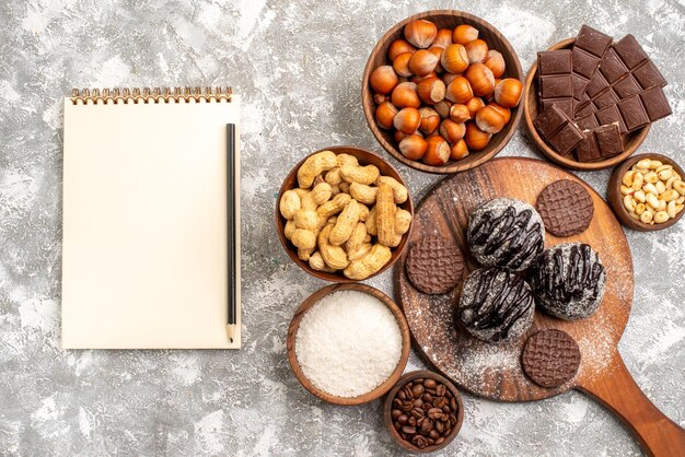 Top view of delicious chocolate cakes with cookies nuts and peanuts on white surface