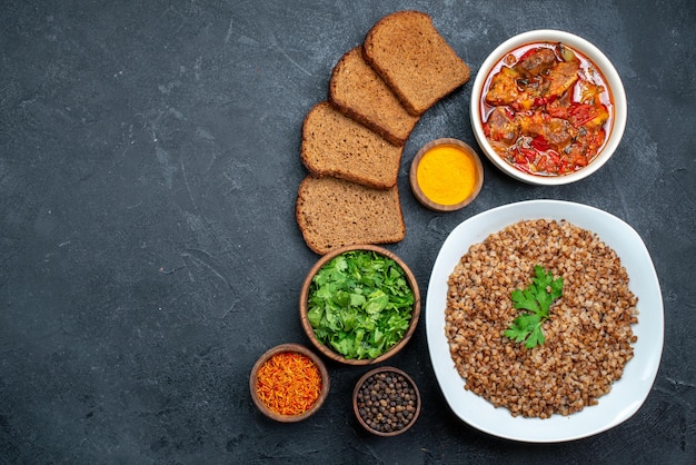 Top view delicious cooked buckwheat with bread and soup on dark space