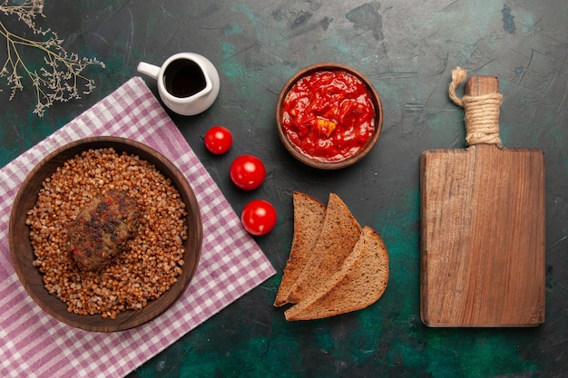 Top view delicious cooked buckwheat with dark bread loafs and cutlet on the dark-green surface ingredient meal food vegetable dish