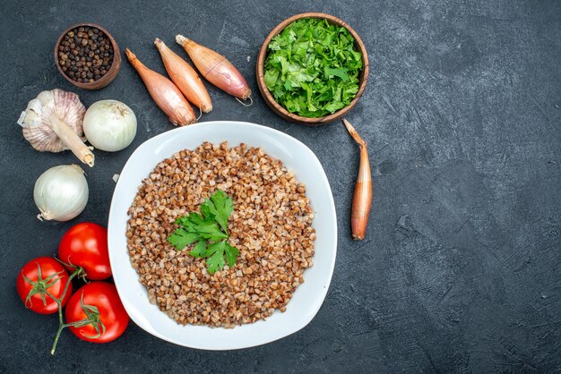 Top view delicious cooked buckwheat with fresh tomatoes and greens on grey space