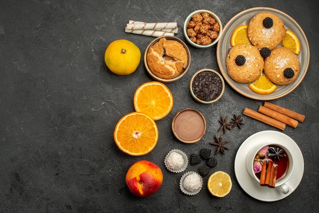 Top view delicious cookies with cup of tea and orange on dark surface tea cookie biscuit cake