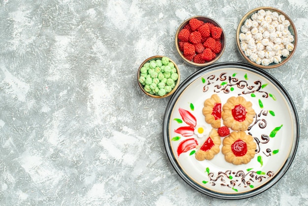 Top view delicious cookies with red jelly and candies on white background biscuit cake cookie sweet