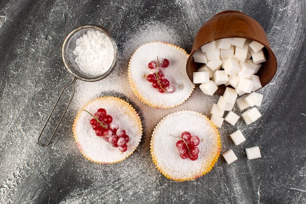 Top view delicious cranberry cakes with red cranberries on top sugar pieces and sugar powder grey desk cake biscuit sweet