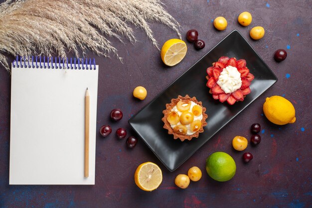 Top view of delicious creamy cakes inside plate with fresh lemons and fruits on the dark surface