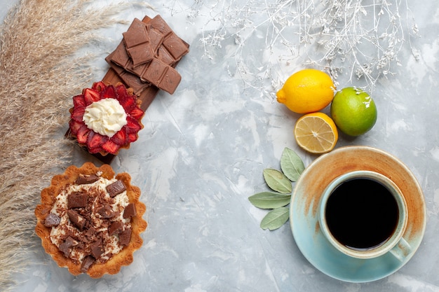 Top view delicious creamy cakes with chocolate bars lemon and tea on the white desk cake biscuit sweet sugar bake