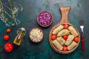 Free photo top view delicious dolma meat meal rolled with cabbage and tomatoes along with oil on dark-blue desk meat food dinner vegetables dish cooking