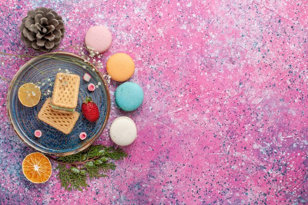 Top view of delicious french macarons with waffles on pink surface