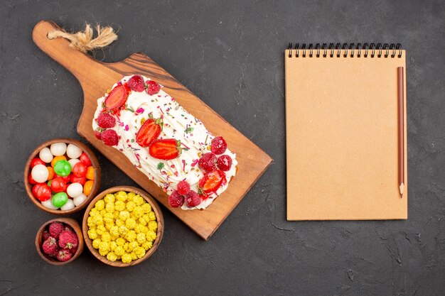 Top view delicious fruit cake with cream and candies on a dark background candy cake biscuit fruit sweet pie