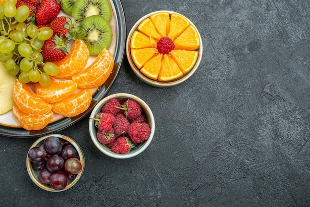 Free photo top view delicious fruit composition fresh and sliced fruits on a dark background health ripe fresh fruit mellow