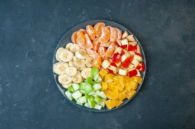 Top view delicious fruit salad sliced tangerines apples bananas and oranges on dark background