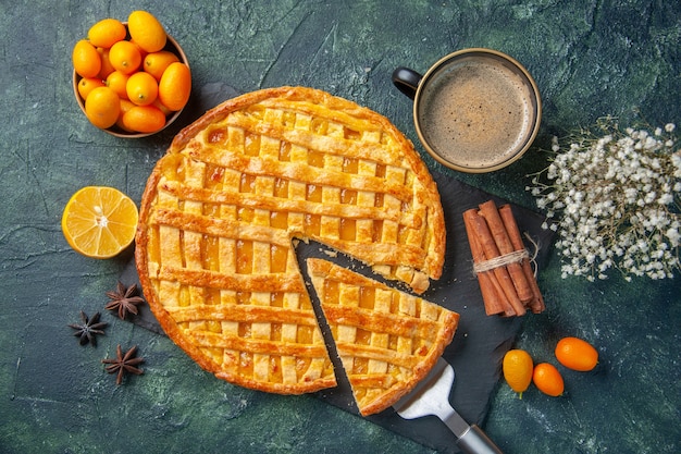 top view delicious kumquat pie with sliced one piece and coffee on dark background