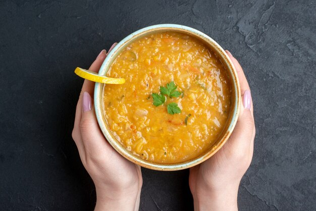 Top view delicious lentil soup with female holding plate and dark bread loafs on dark surface