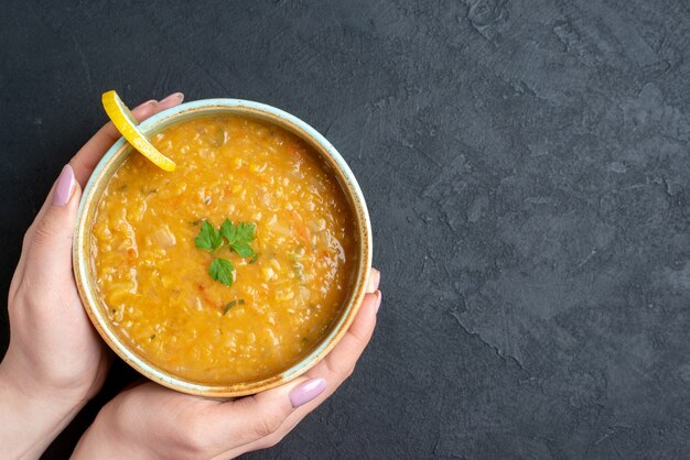 Top view delicious lentil soup with female holding plate on a dark surface