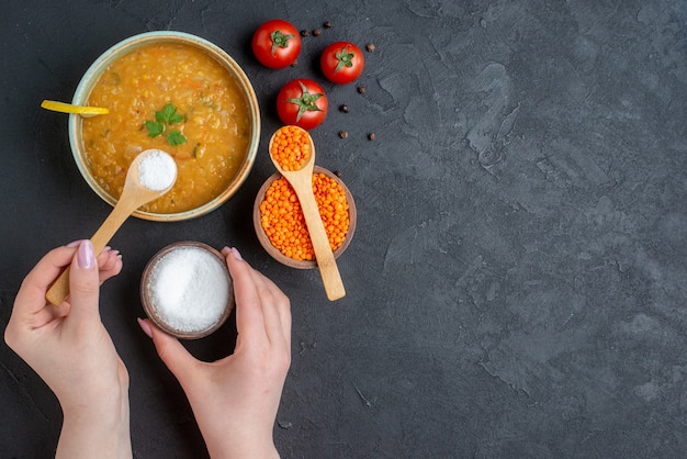 Top view delicious lentil soup with female whose pouring salt into her soup on dark surface