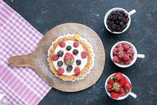 Free photo top view of delicious little cake with sugar powder cream and berries along with cups of berries on dark desk, berry fruit cake biscuit