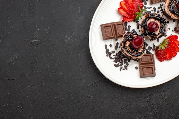 Free photo top view delicious little cakes with chocolate bars and strawberries on a dark background pie chocolate cocoa cake sweet tea