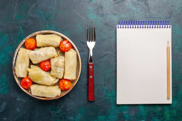 Free photo top view delicious meat meal rolled inside cabbage with tomatoes and notepad on the dark-blue desk meat food dinner calories vegetable cooking