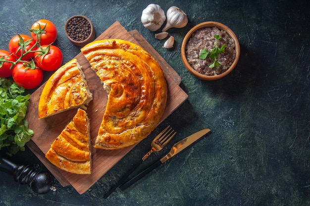 Top view of delicious meat pie with ingredients on dark surface