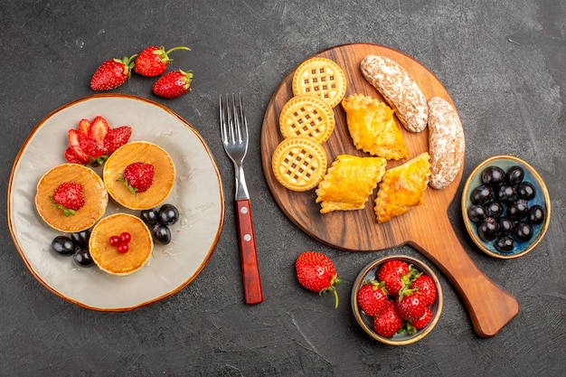 Top view delicious pancakes with fruits and cookies on dark surface cake fruit sweet pie