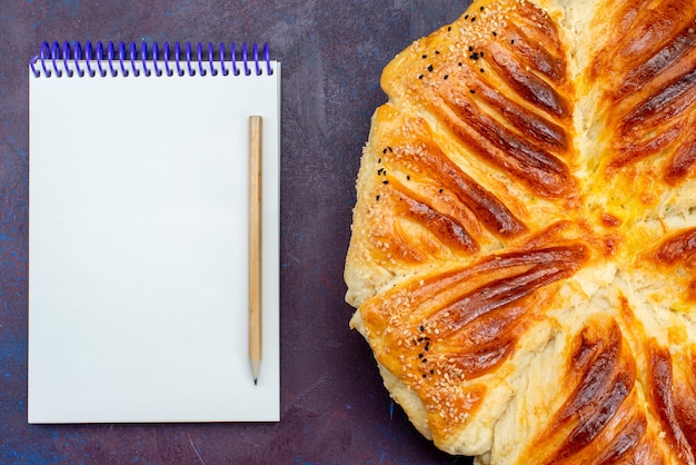 Free Photo top view delicious pastry baked bun formed pastry with notepad on the dark background.